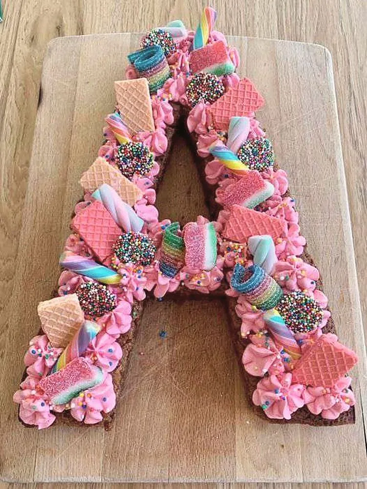 A letter-shaped cake covered in pink buttercream, sprinkles, wafer biscuits and sweets